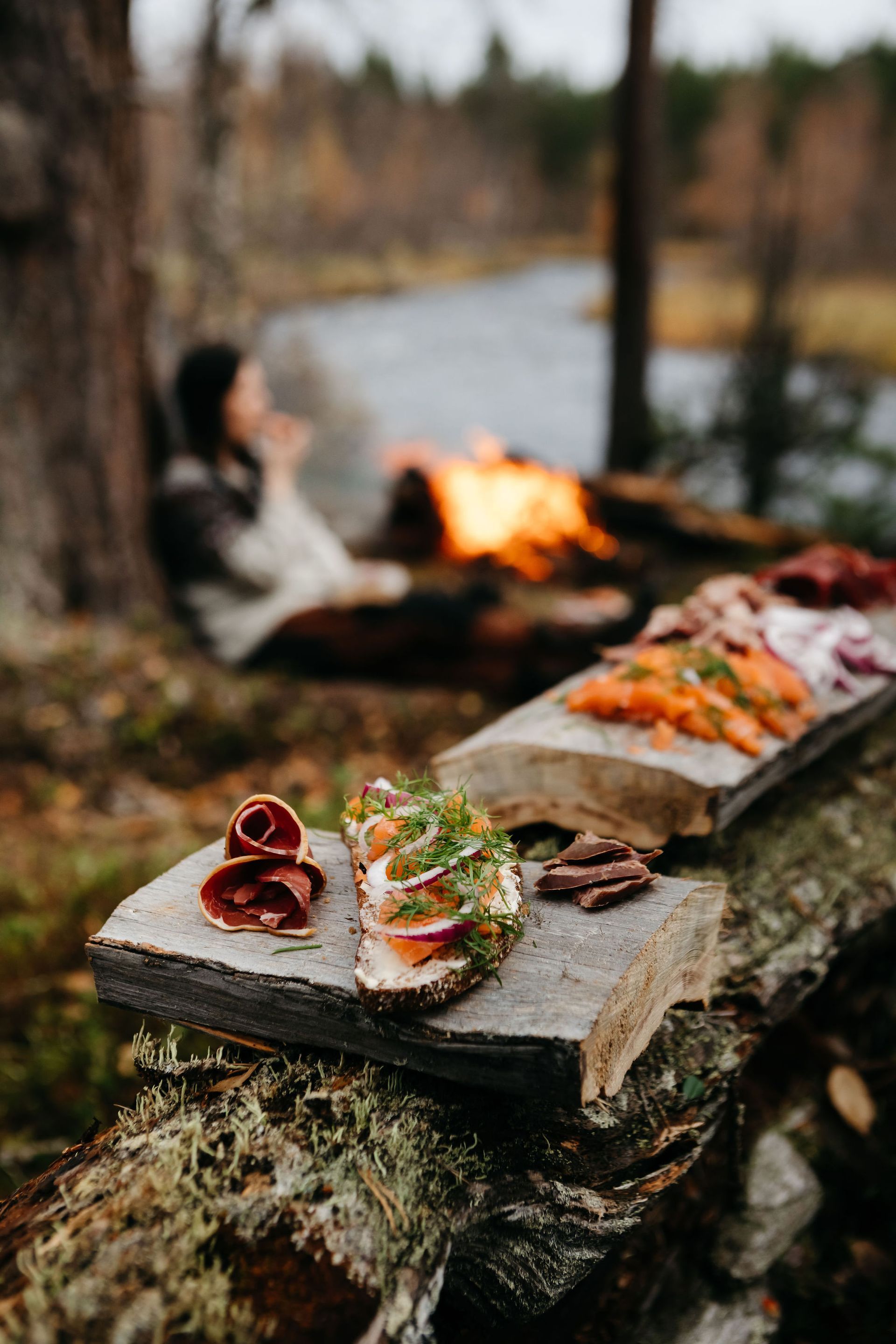 A wooden cutting board with food on it is sitting on a log next to a fire.