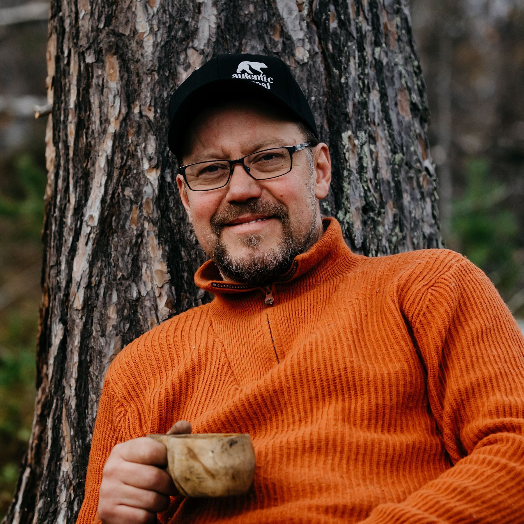 A man leaning against a tree holding a cup of coffee