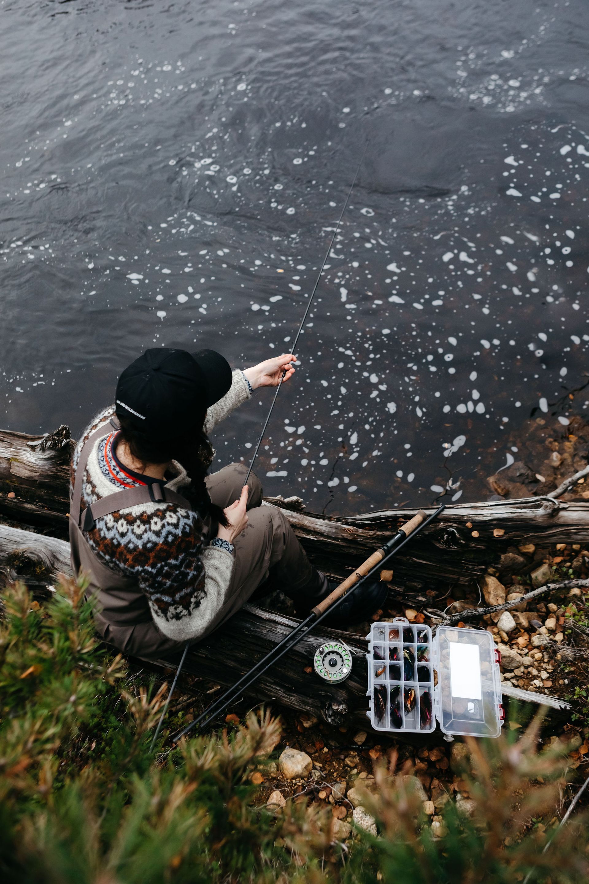 A woman is sitting on a log fishing in a river.