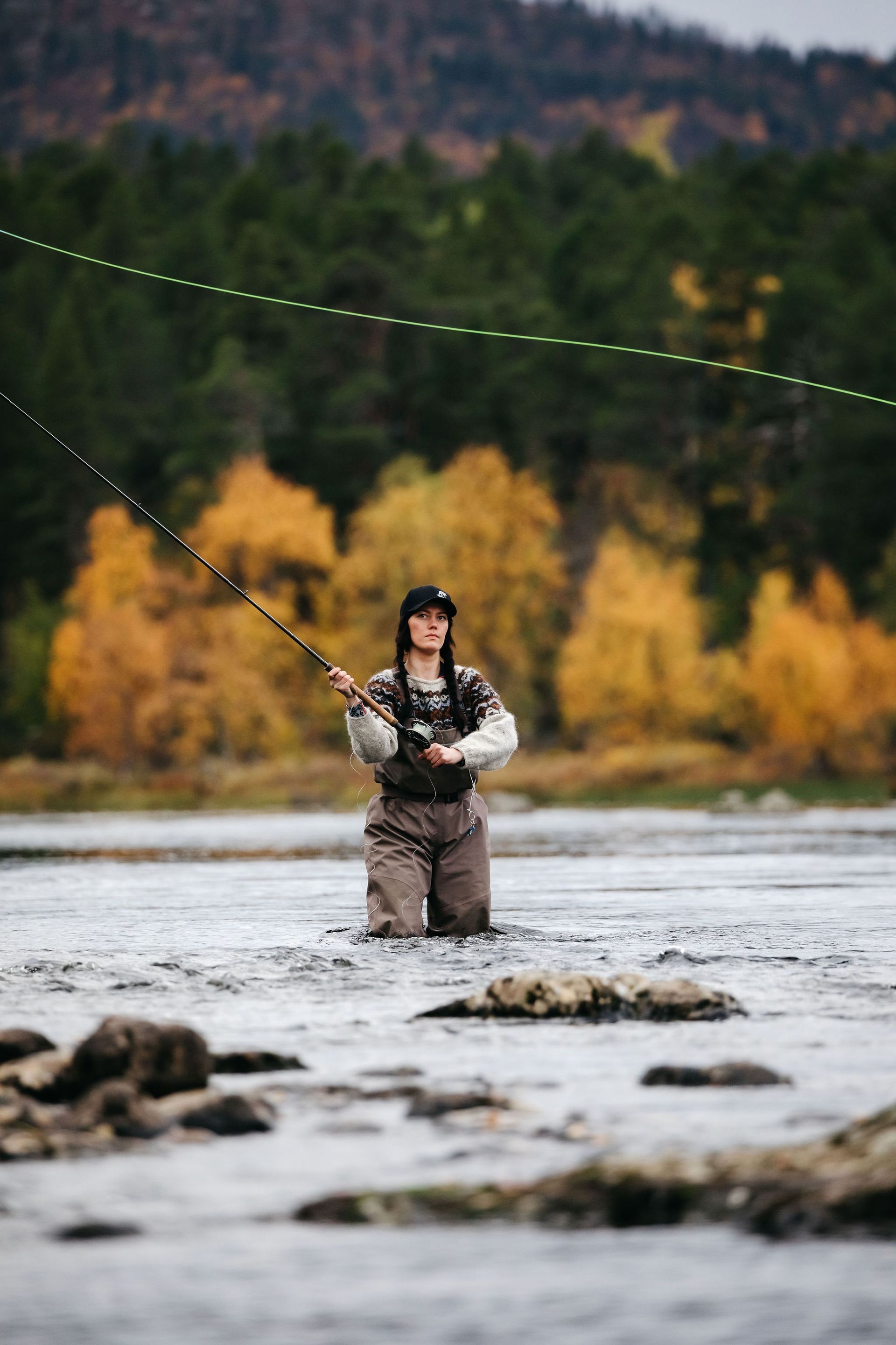 A man is kneeling in a river holding a fishing rod.