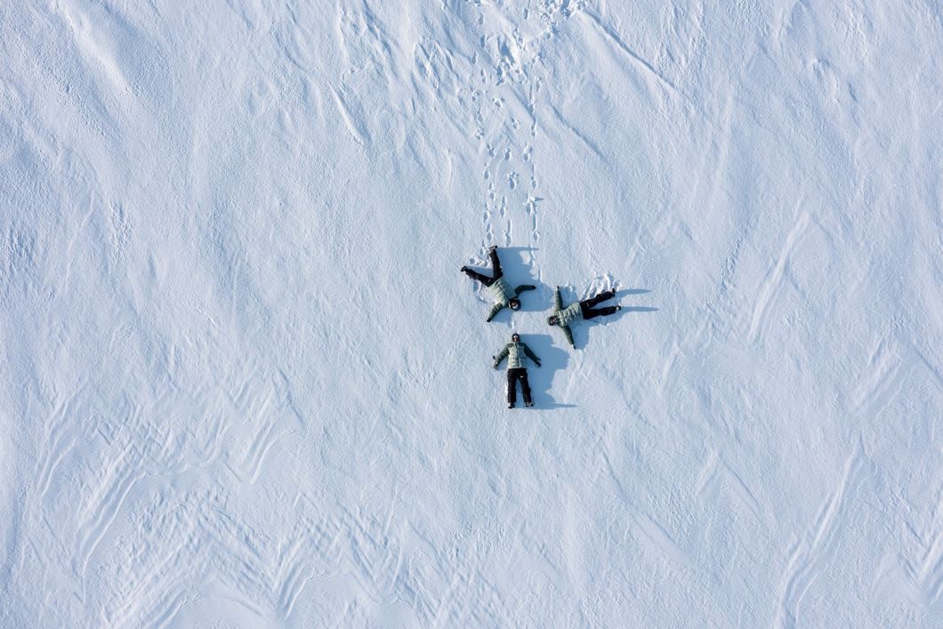 Four people making snow angels in a snowy field.