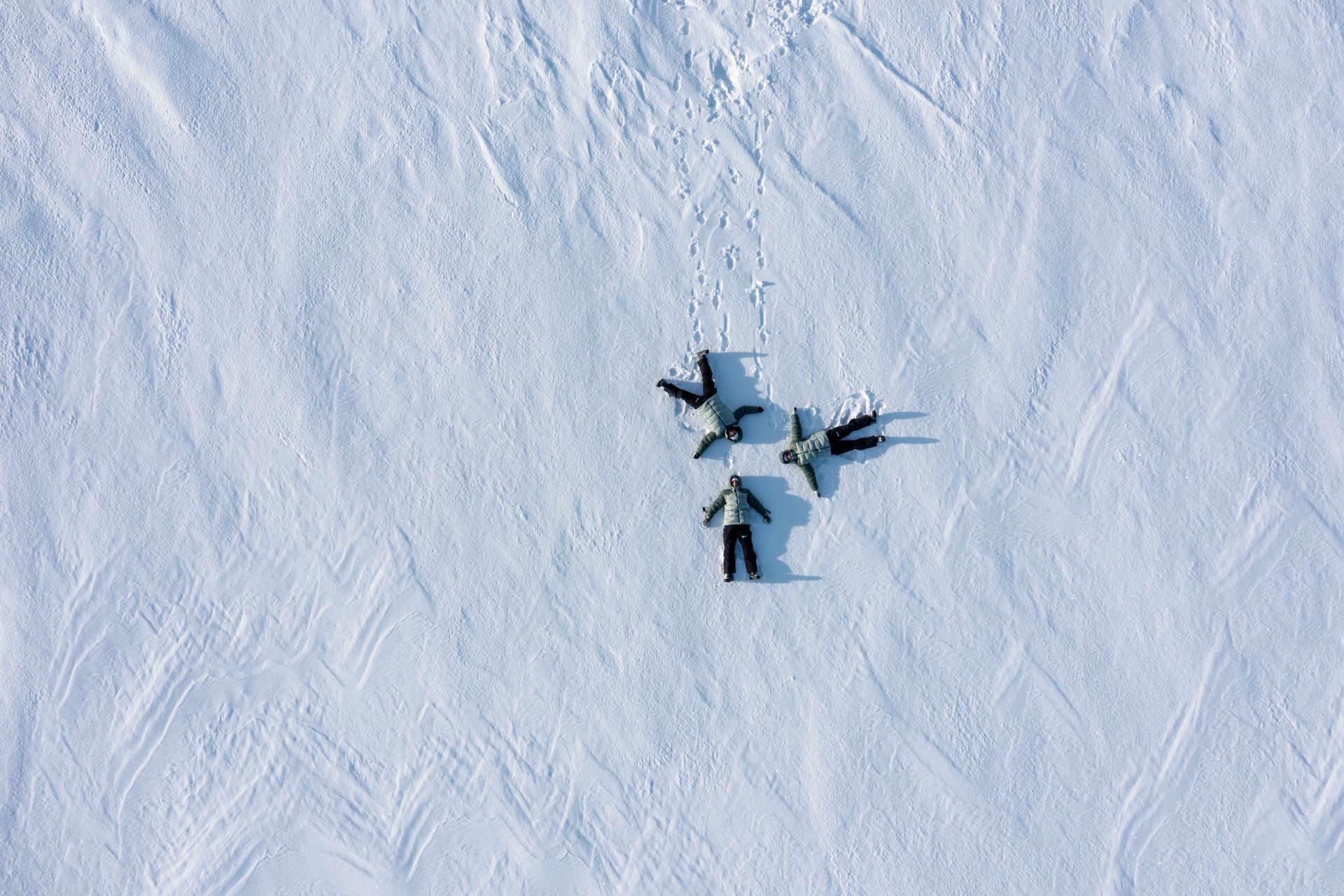 Four people making snow angels in a snowy field.