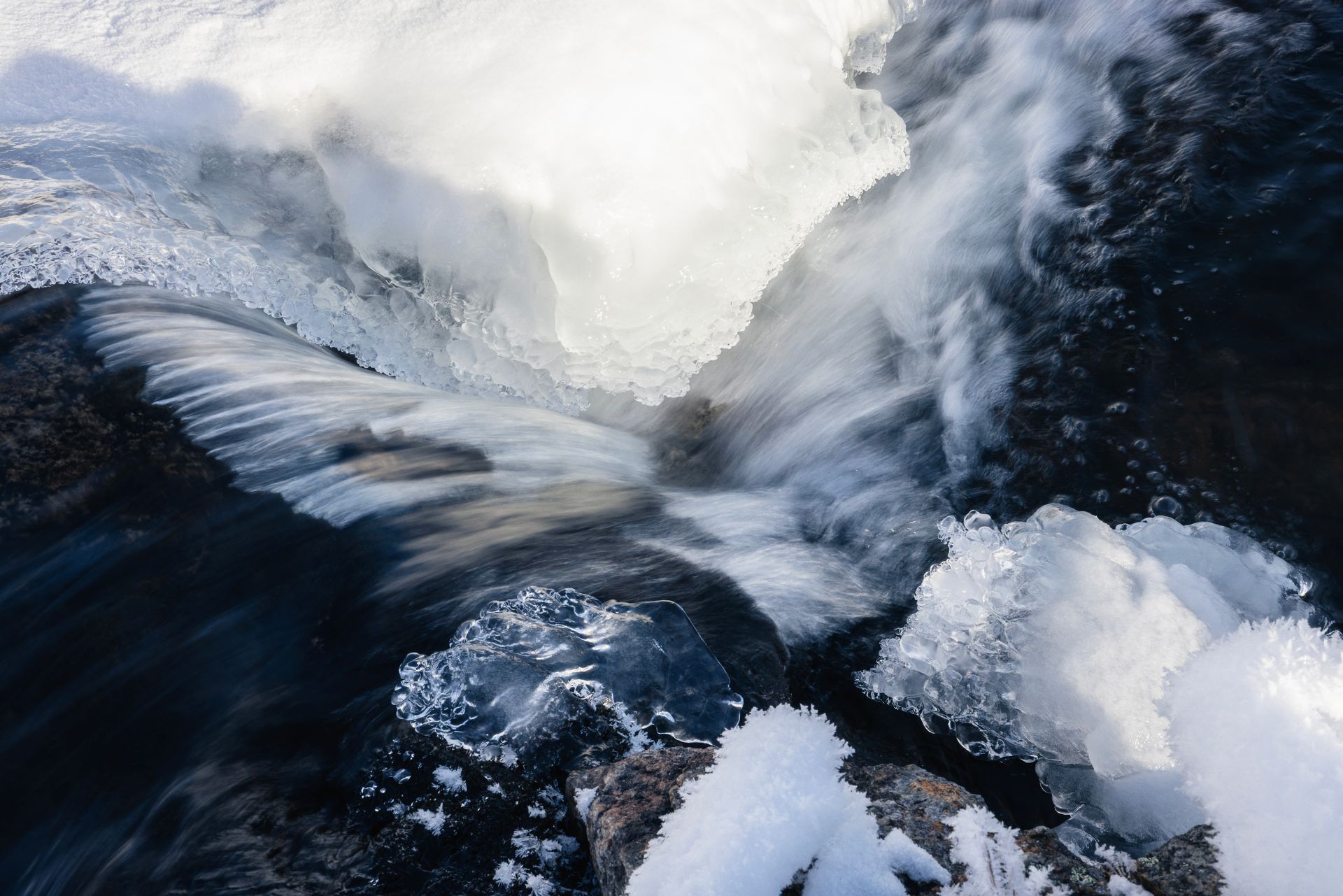 Water flowing through ice and snow, creating a bright, textured cascade in a winter scene.
