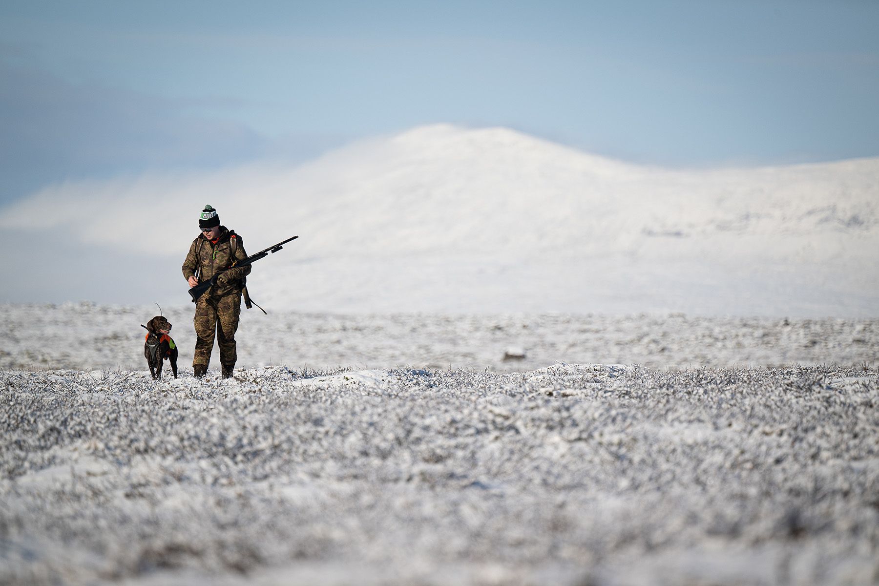 A man and a dog are walking through a snowy field.