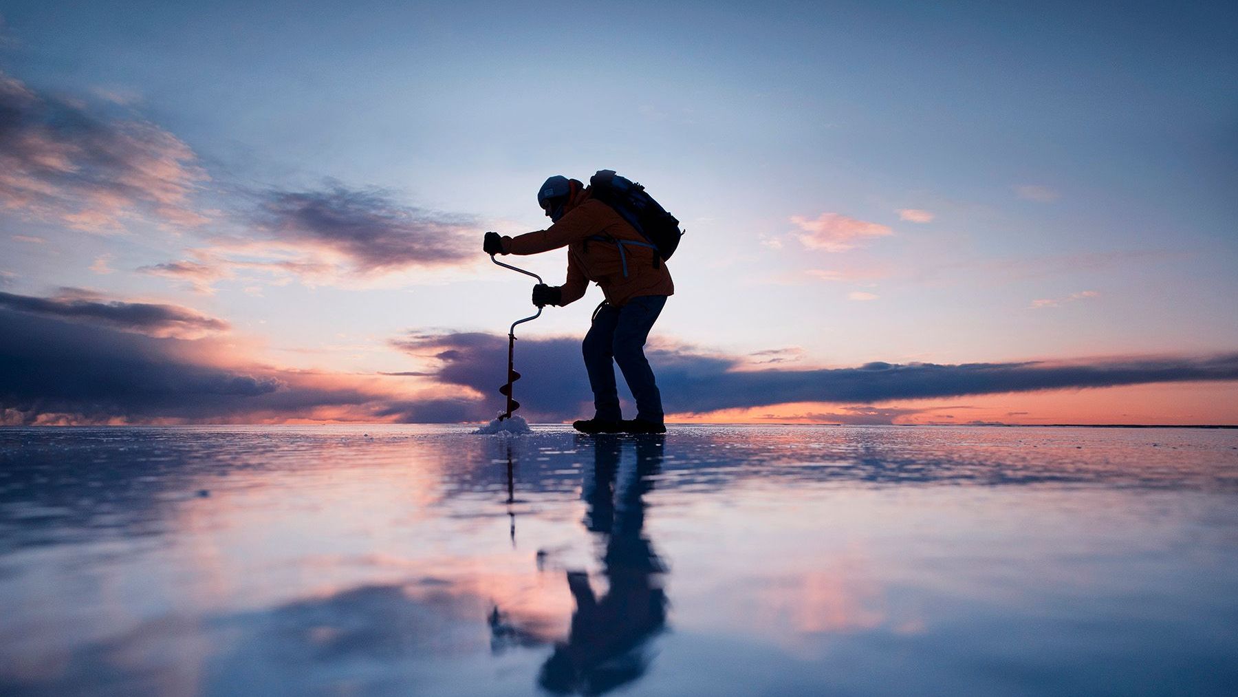 A man is standing on a frozen lake holding a fishing rod.