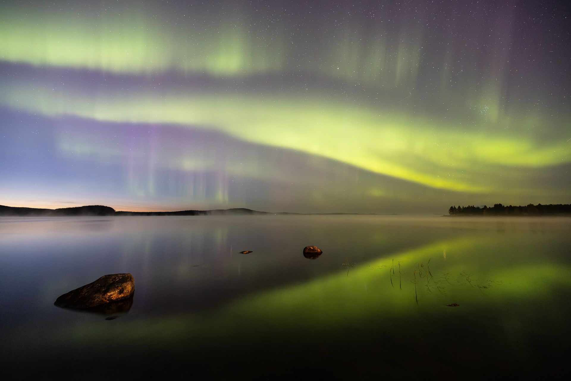 The aurora borealis is reflected in the water of a lake.
