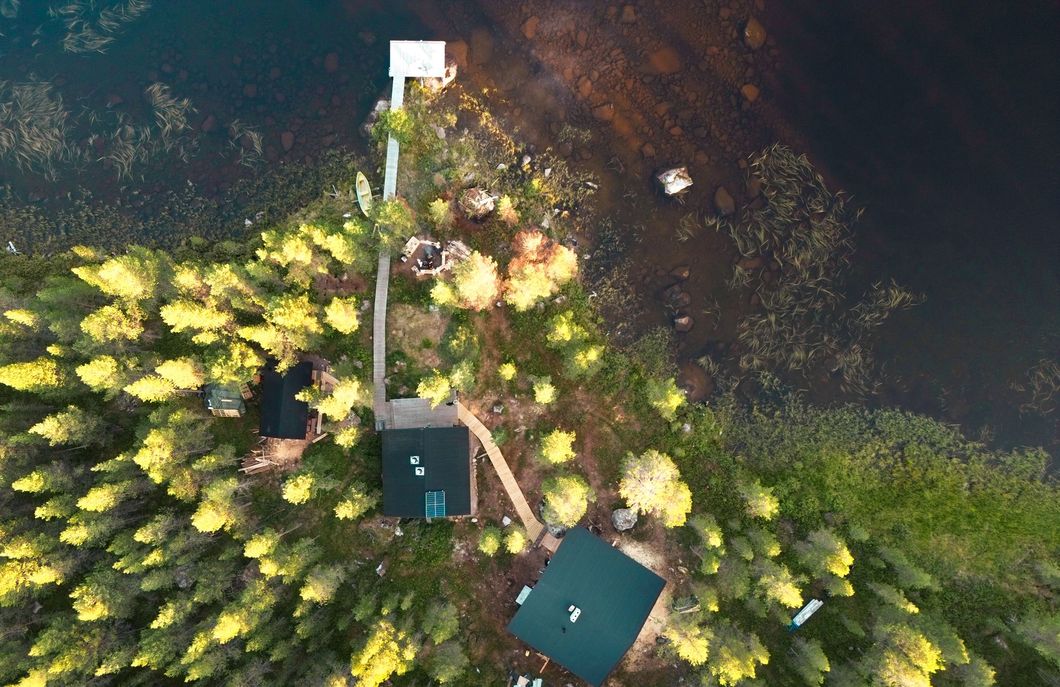 Aerial view of cabins and dock on a wooded shoreline next to a dark lake; golden sunlight.