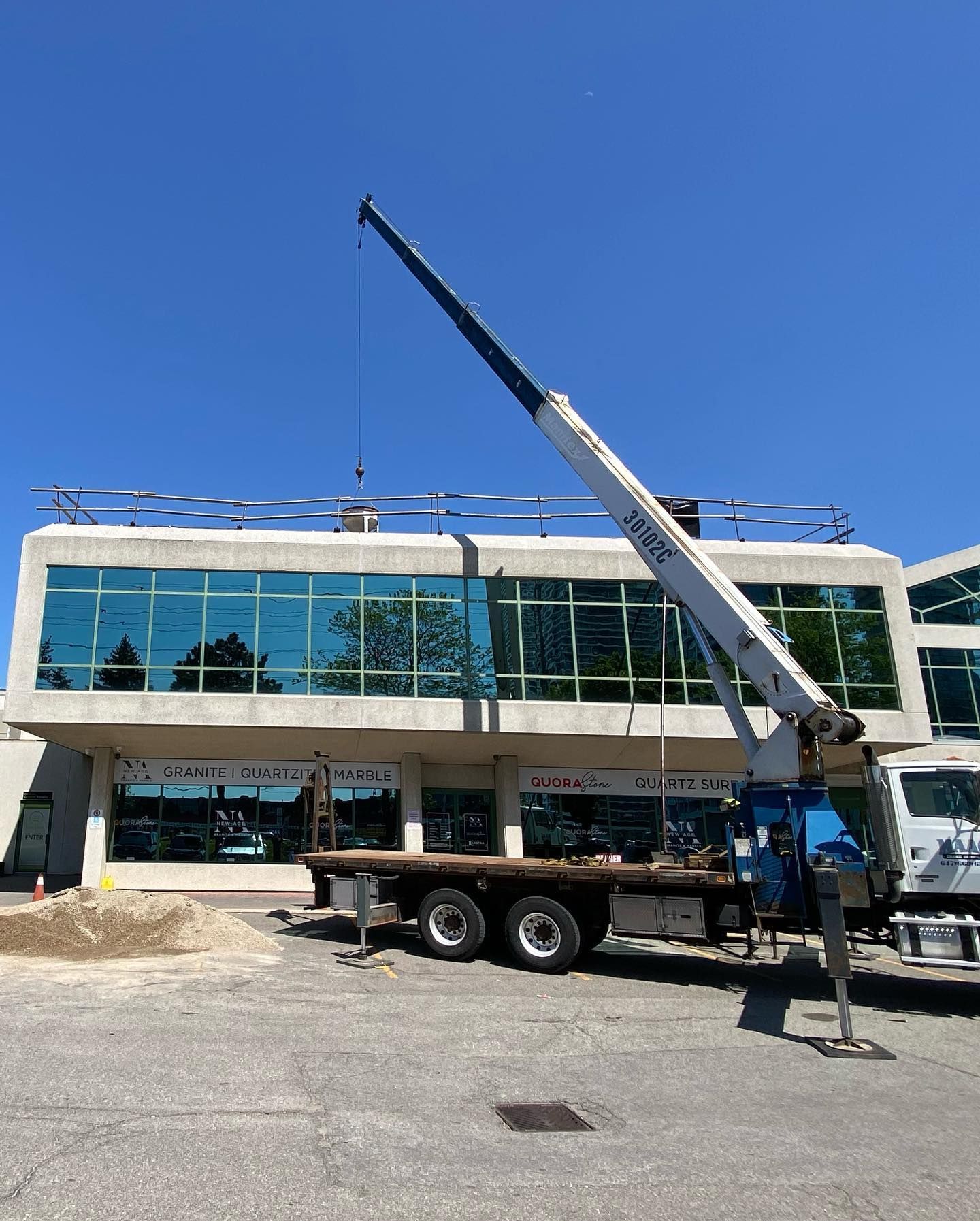 A white crane truck parked in front of a modern office building with blue reflective glass windows under a clear sky.