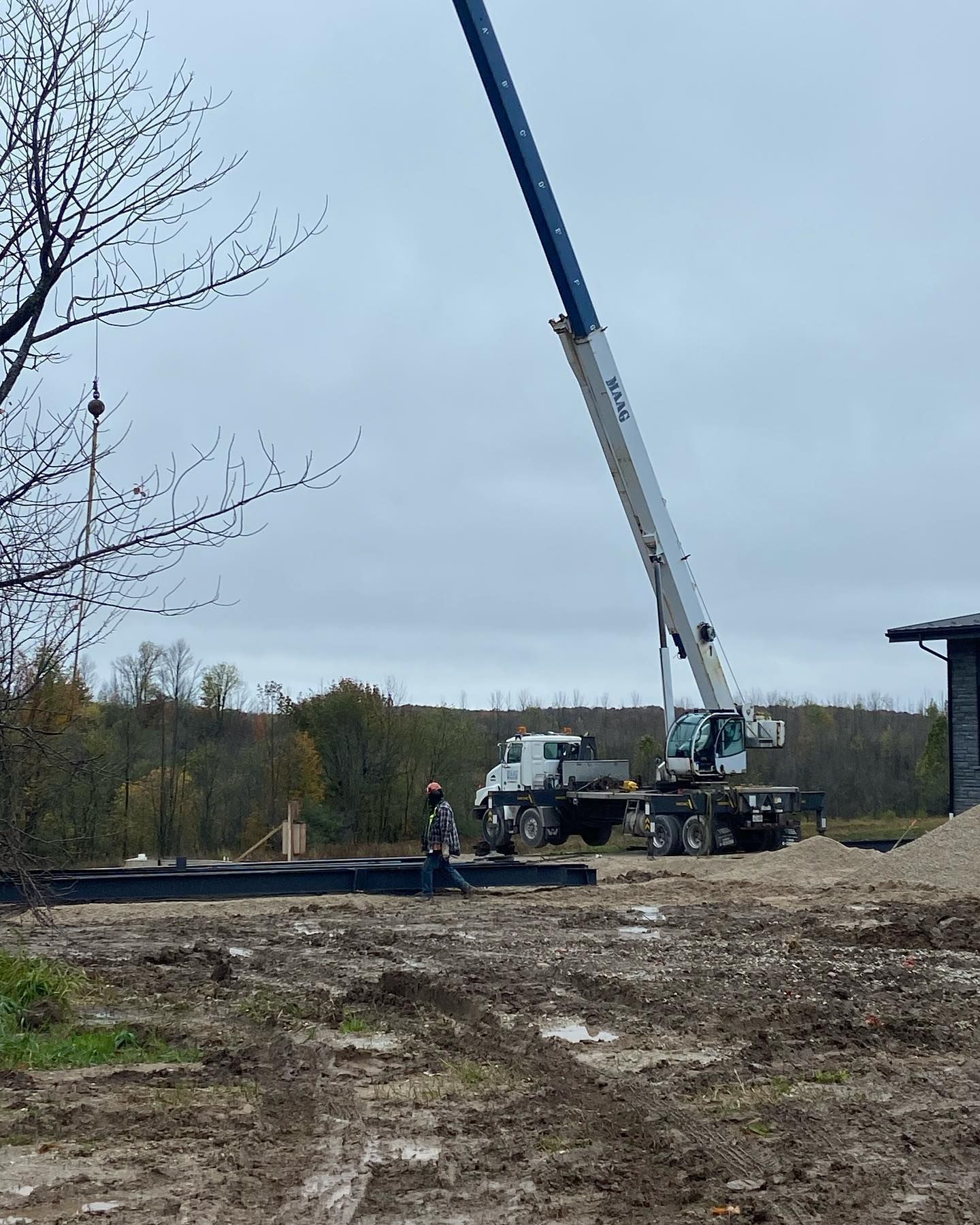 A construction crane stands on a muddy, outdoor site with a worker walking near black landscape fabric.