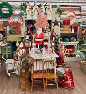 Festive holiday display with Santa figure, red decorations, chairs, and potted plants in a shop interior