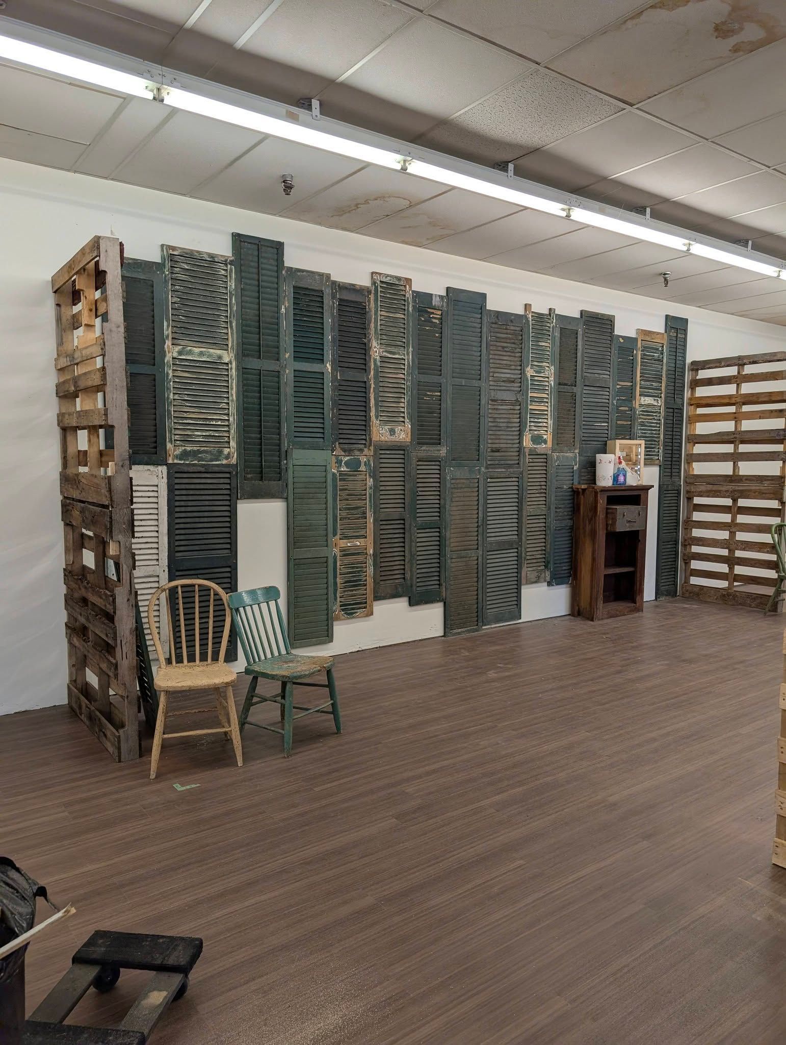 Empty room with stacked display panels, chairs, and shelving on a wood floor.