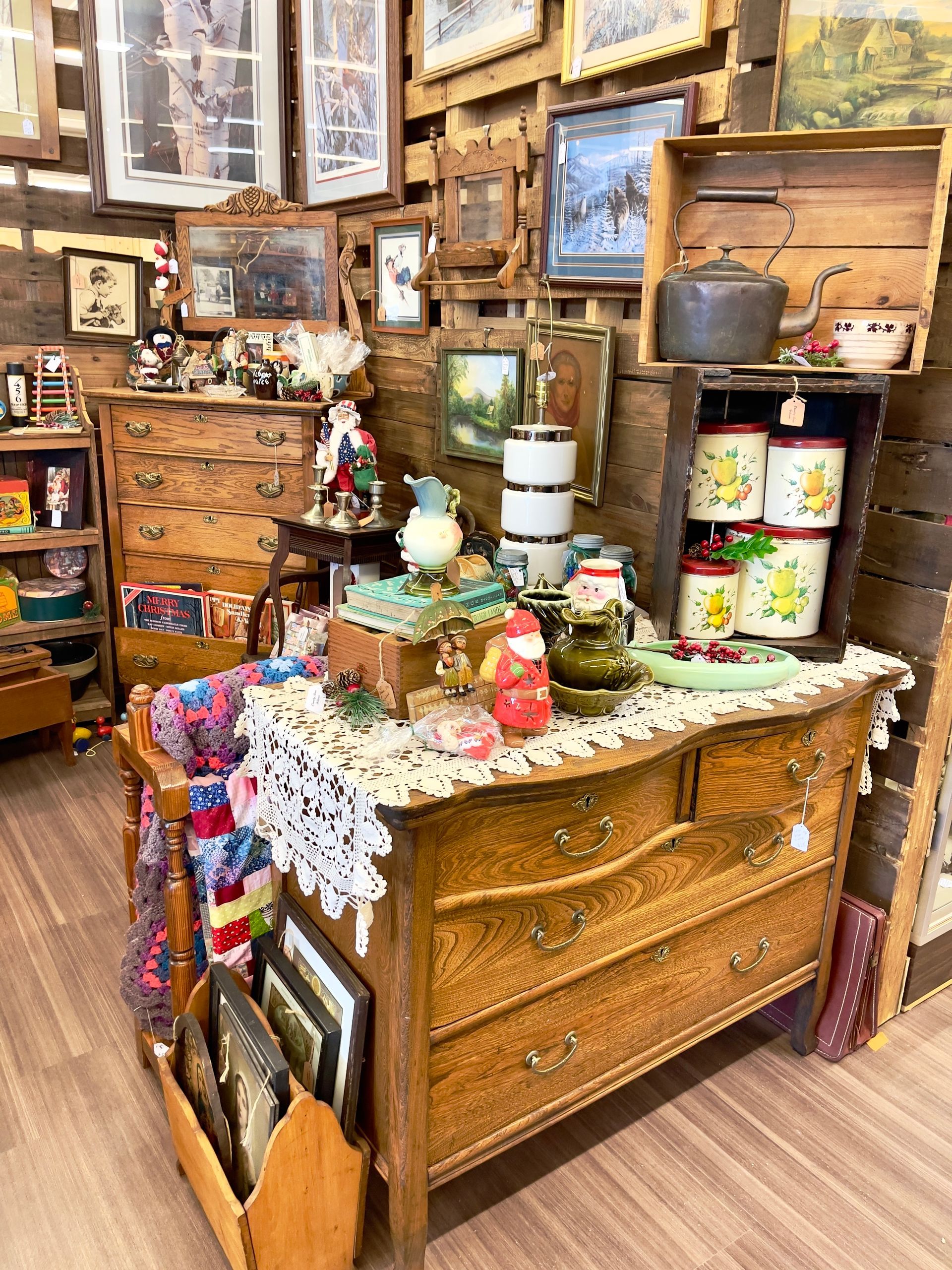 Antique shop display with vintage dressers, framed art, and colorful ceramic containers.