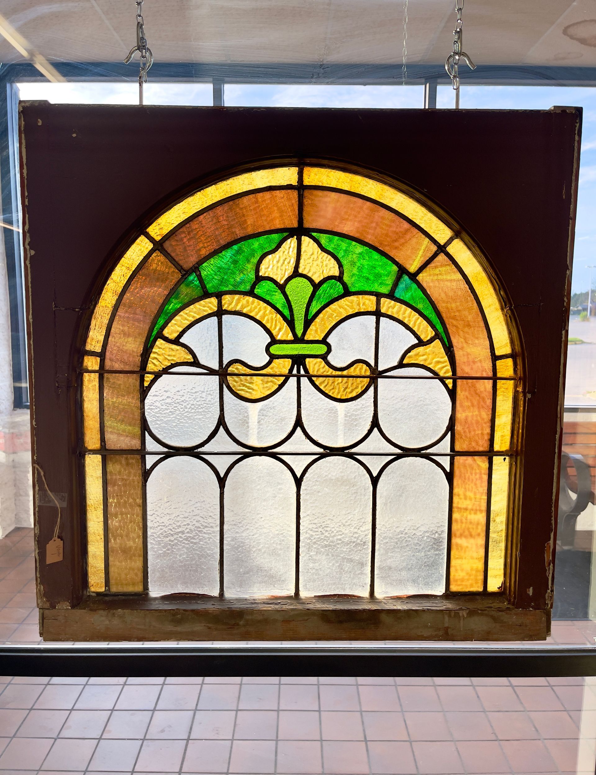 Stained glass window panel with green, amber, and white arches hanging indoors.