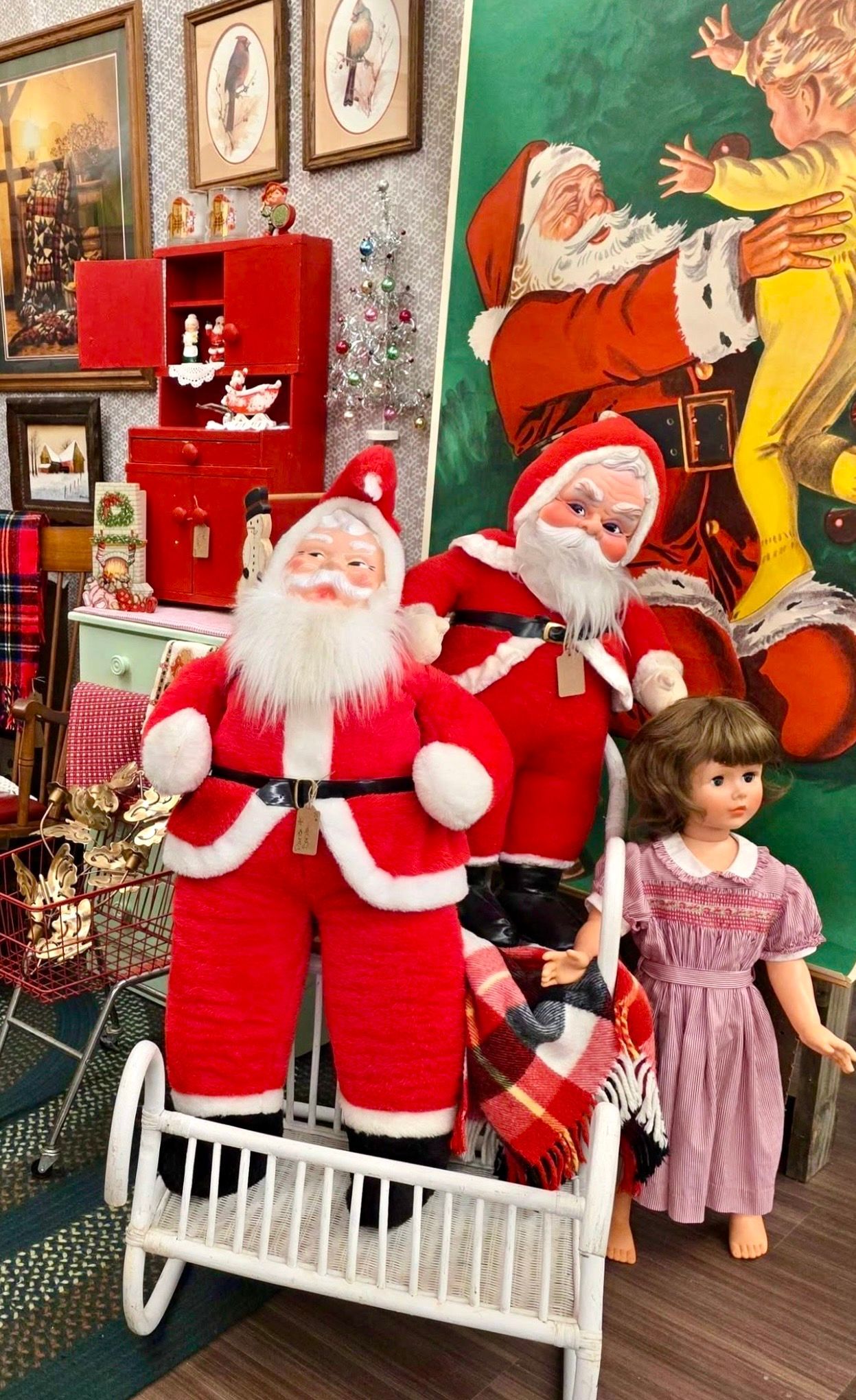 Santa figures in a holiday display with a child standing beside them and framed portraits on the wall