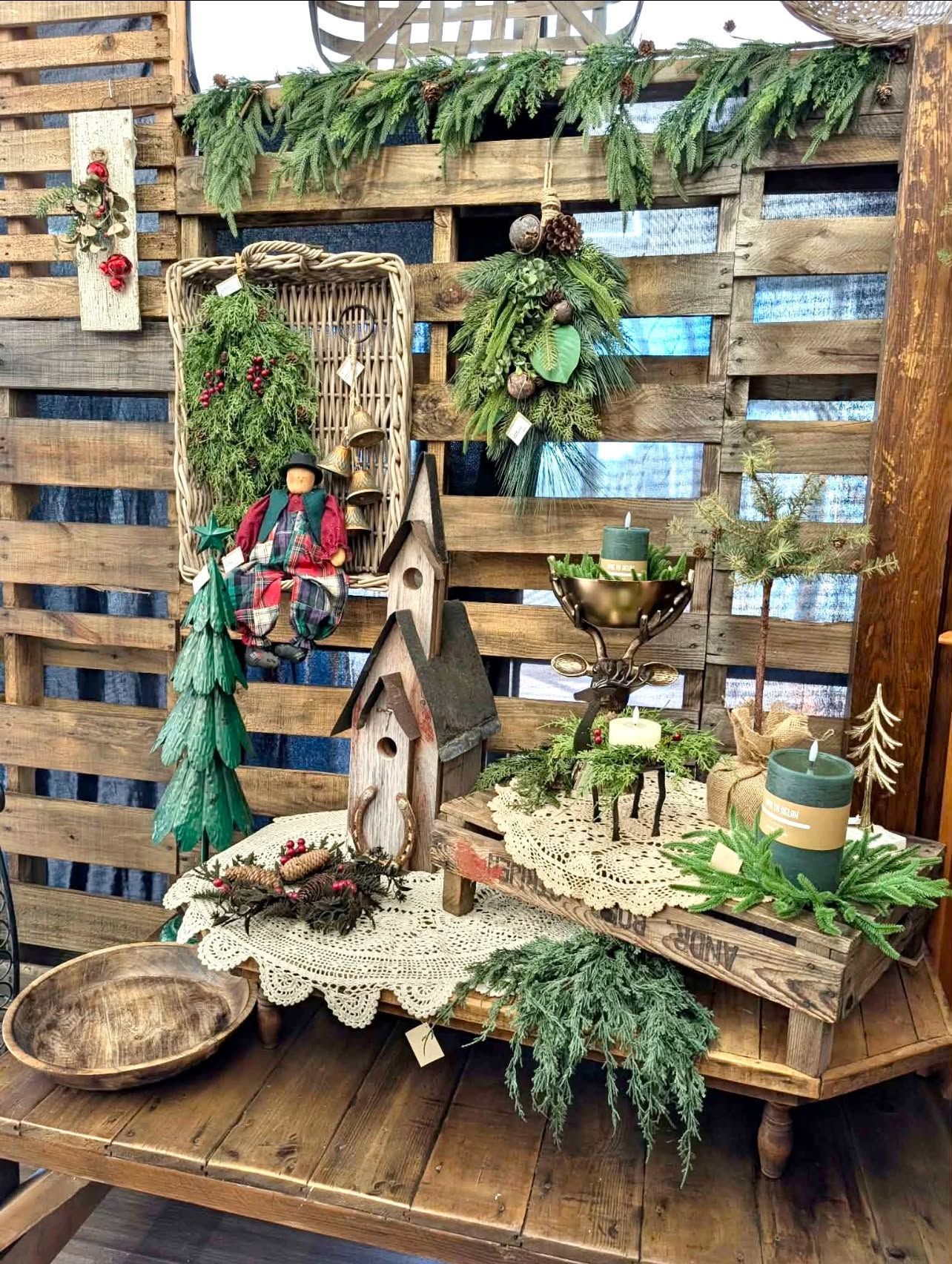 Rustic holiday display with miniature wooden houses, wreaths, greenery, and candles on a wooden shelf