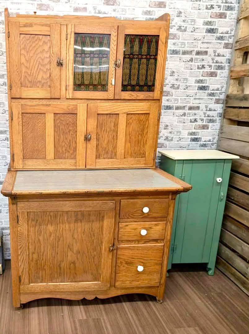 Wooden hutch with cabinet and drawers beside a green side cabinet on a wood floor, against a brick wall.