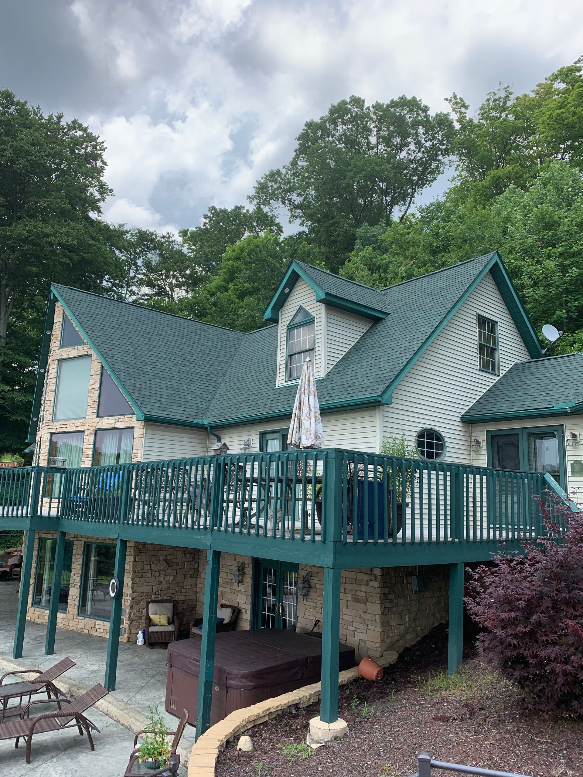 Green-roofed cottage-style treehouse deck amid trees and cloudy sky