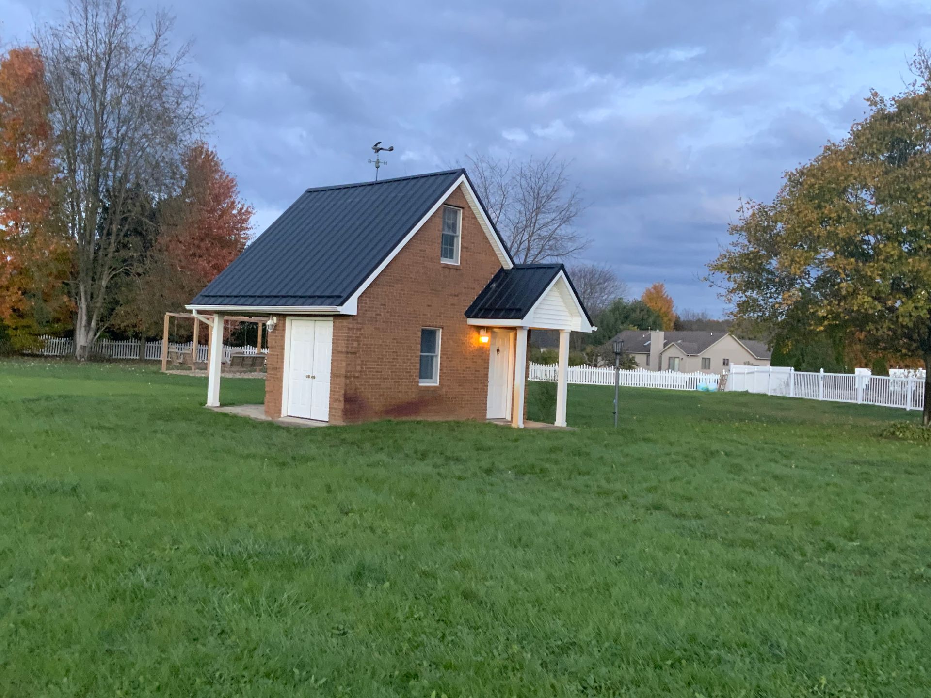 Small brick cottage with dark roof and white trim in a grassy yard under a cloudy sky.