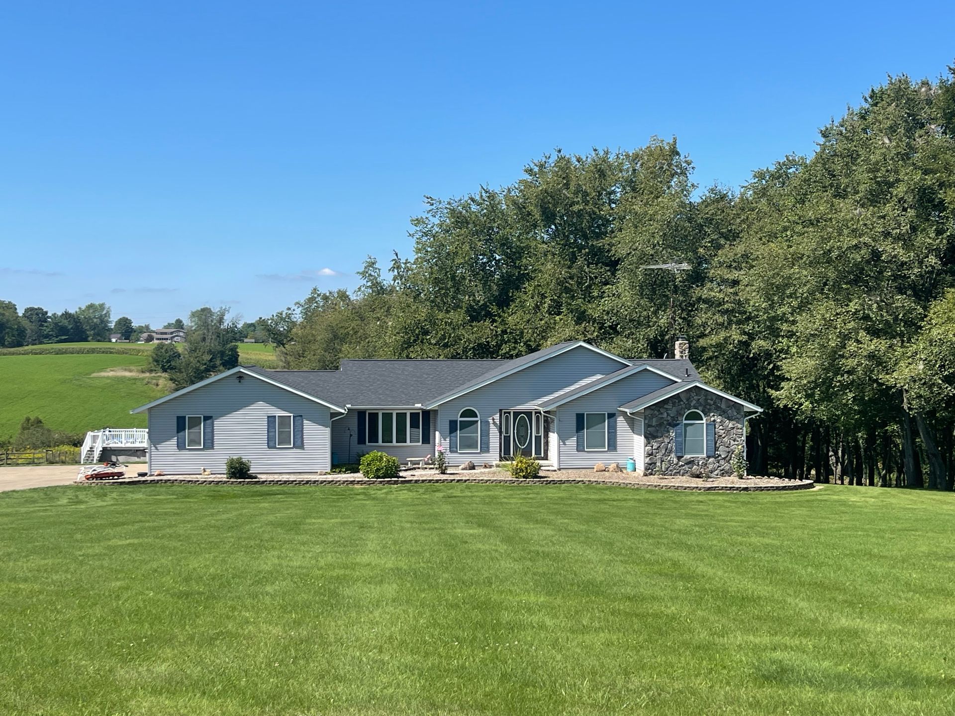 Single-story gray house with a large green lawn under a clear blue sky