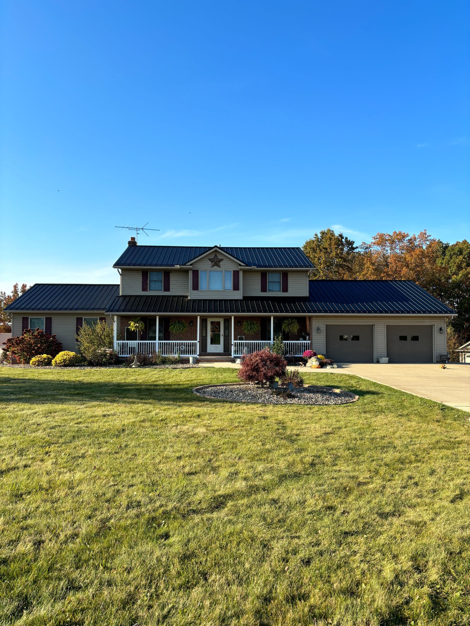 Two-story suburban house with a large lawn, driveway, and clear blue sky.