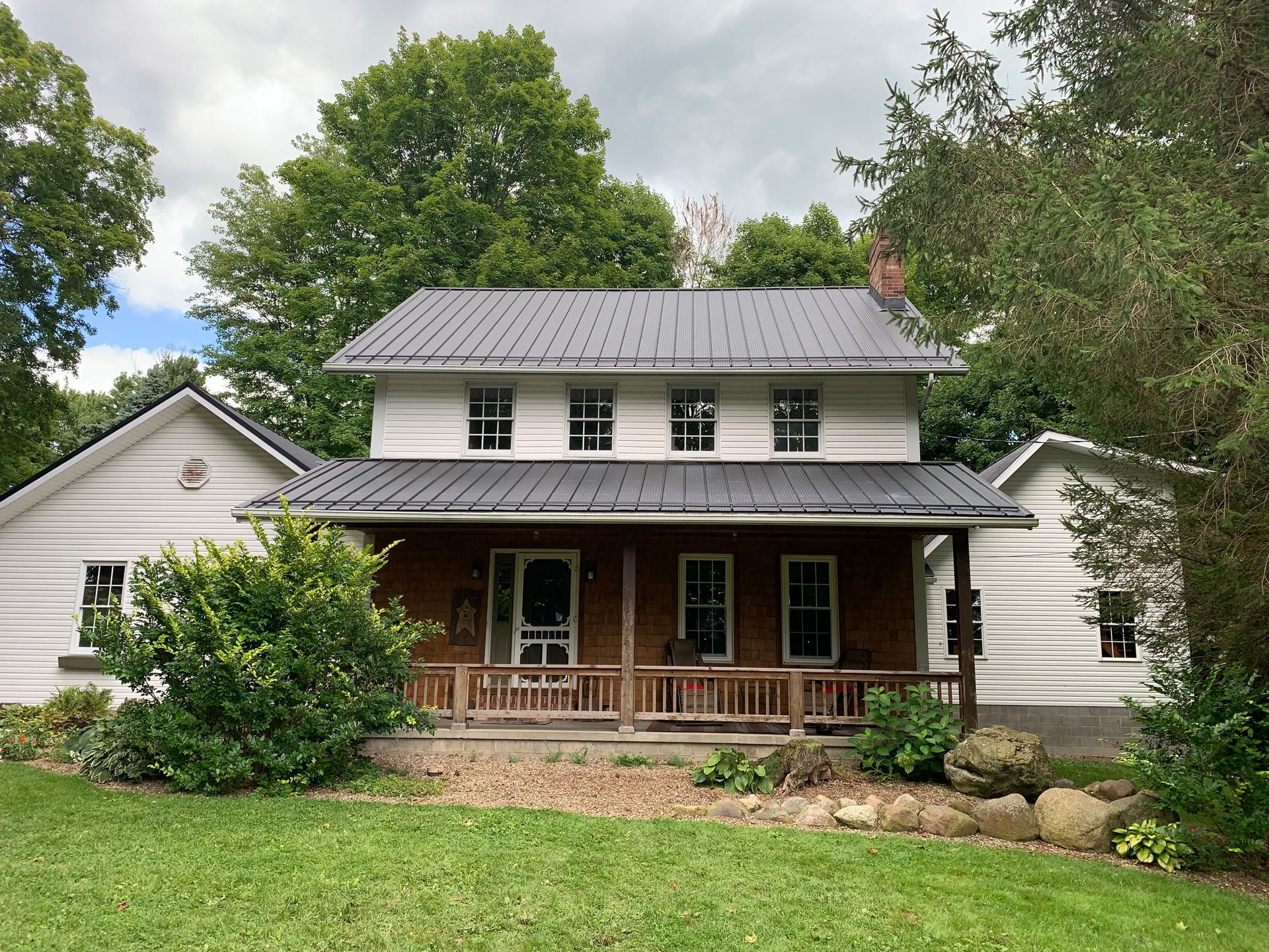 Two-story white house with a covered front porch and large trees in the yard