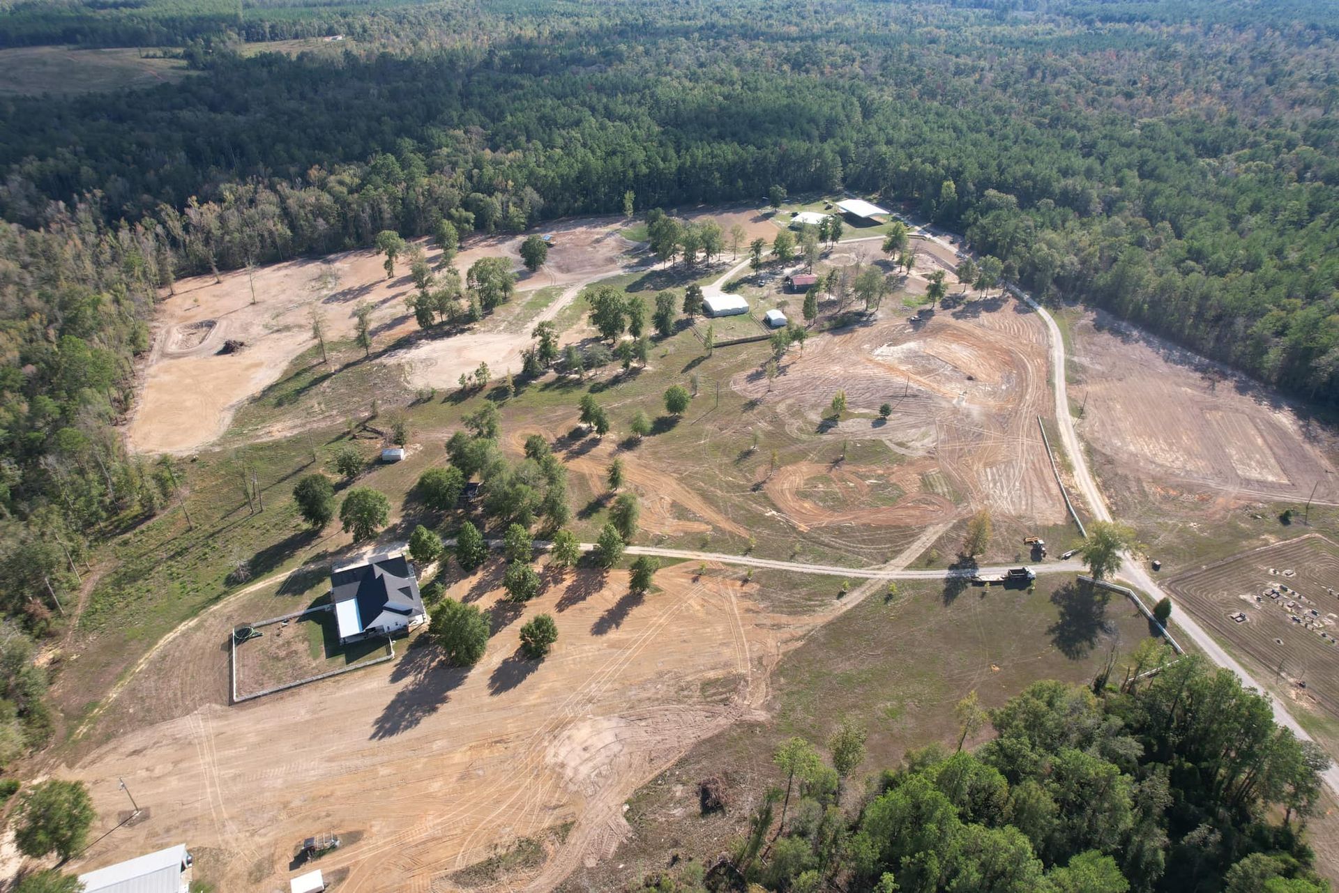 Aerial view of a rural property with a house, cleared land, and surrounding trees.