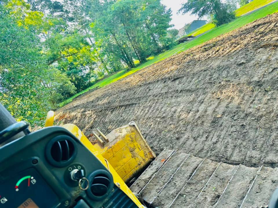 Yellow bulldozer on muddy hillside, preparing ground. Green trees in background.