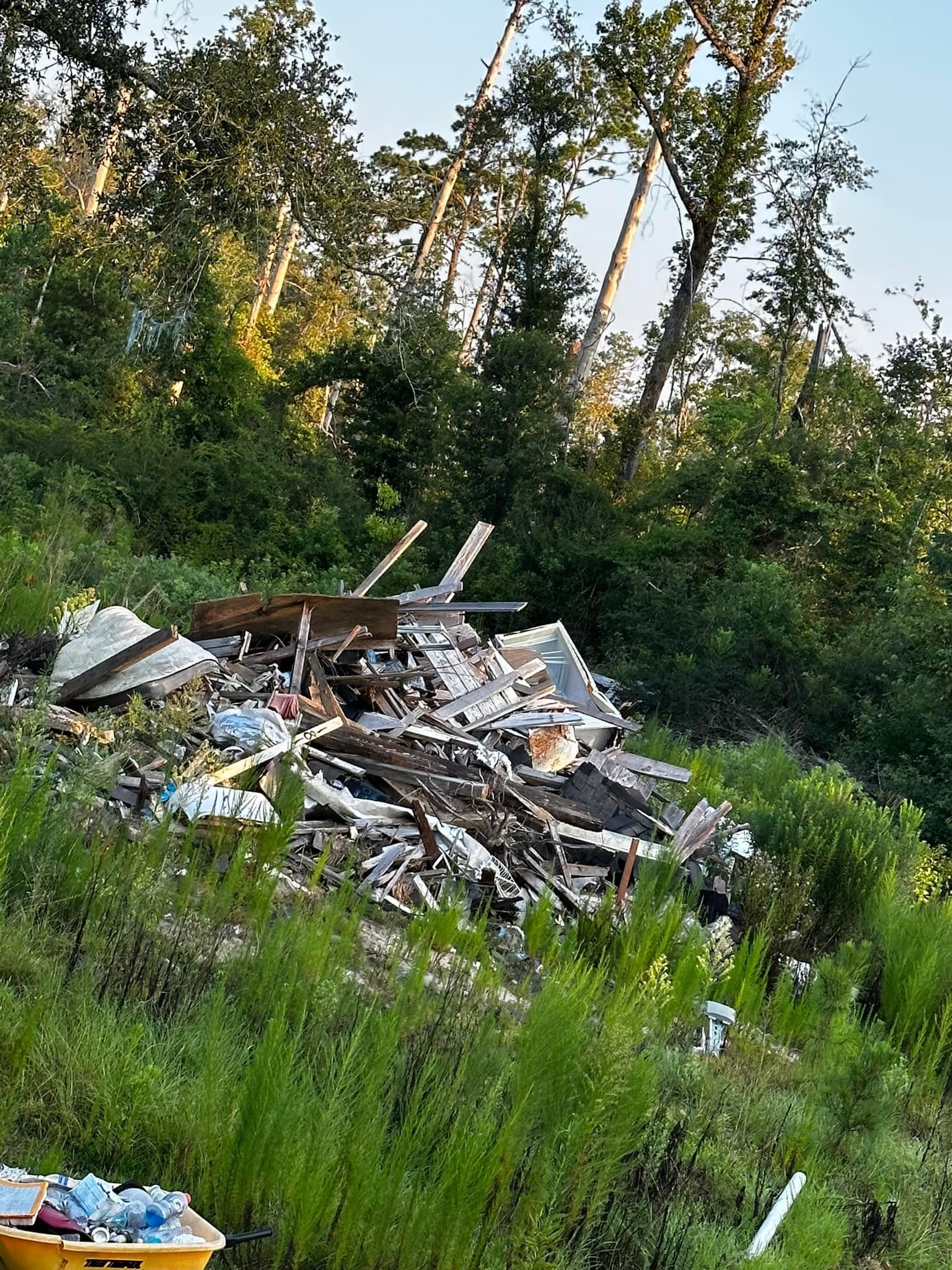 Pile of discarded construction debris on a grassy hillside, with trees in the background.