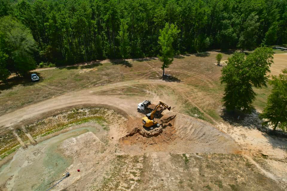 Construction site with excavators on a dirt mound, trees in the background, blue sky.