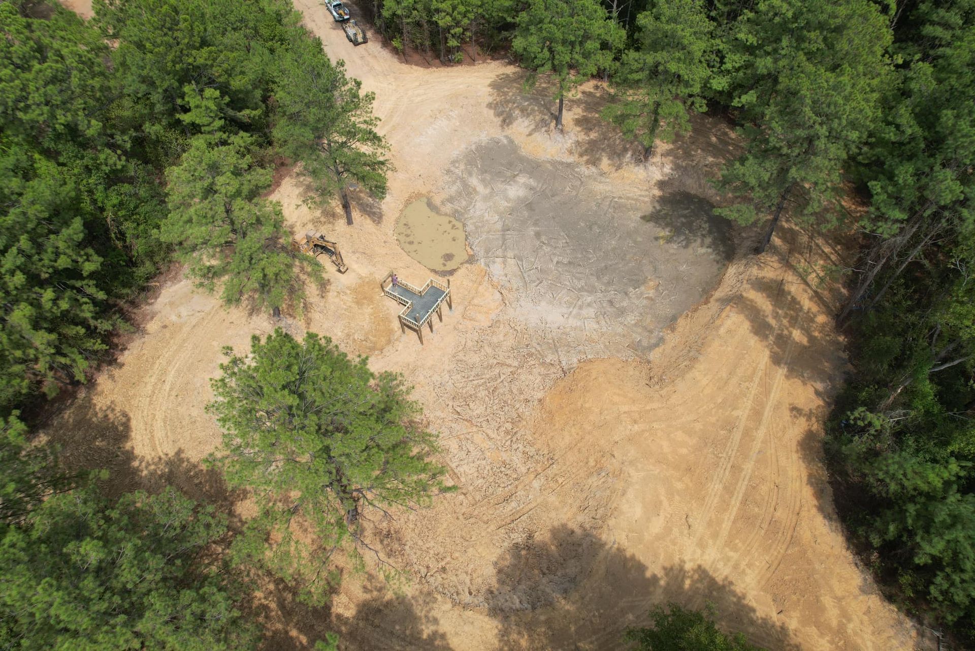 Aerial view of a clearing with a partially dry pond and several people gathered around a structure.