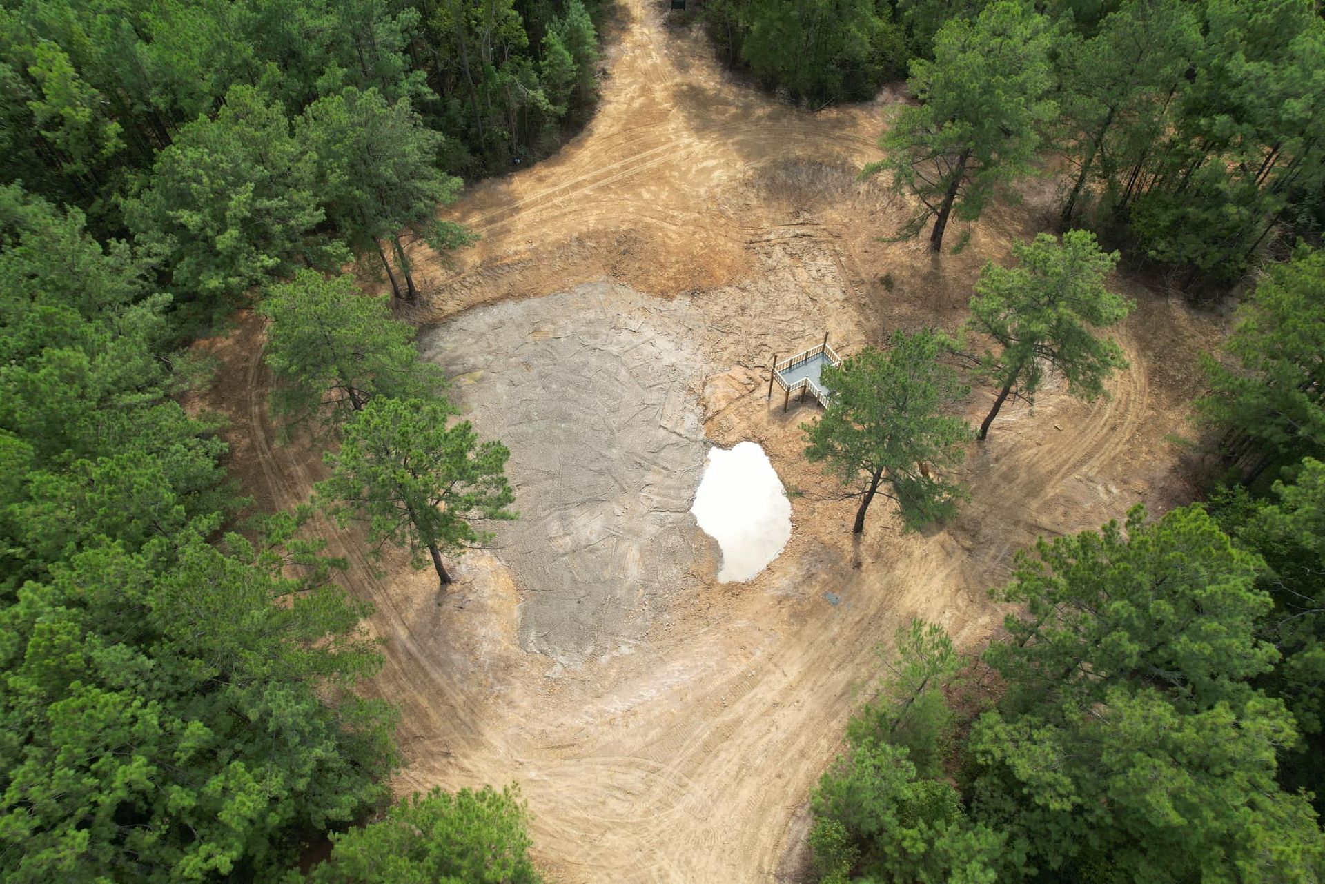 Aerial view of a clearing in a forest, with a gravel area and some trees.