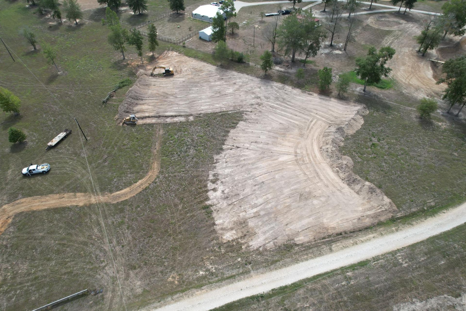 Aerial view of land clearing for construction, showing dirt paths and machinery on a hillside.
