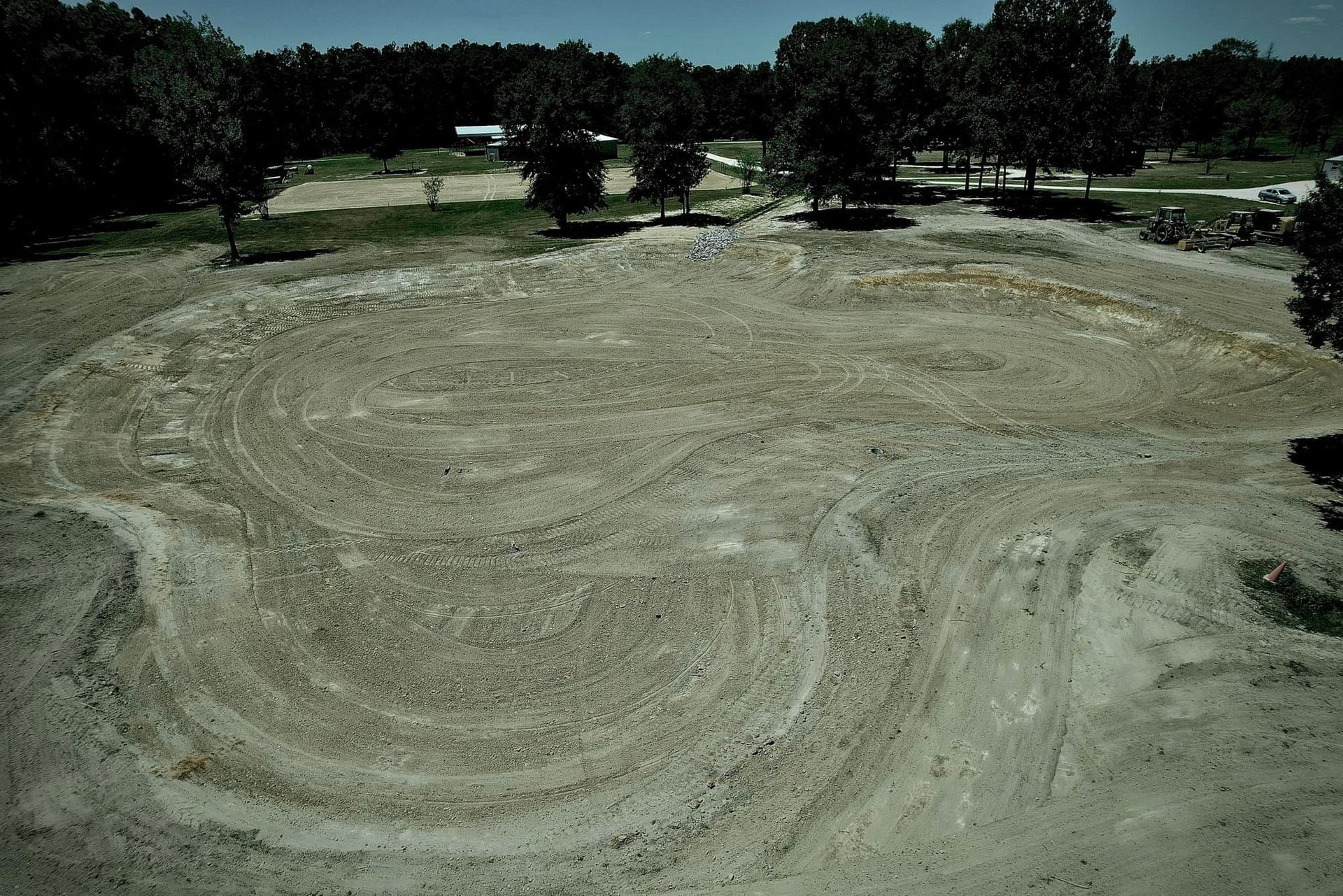 Overhead view of dirt circle with curved tire tracks. Trees and a building in the background.