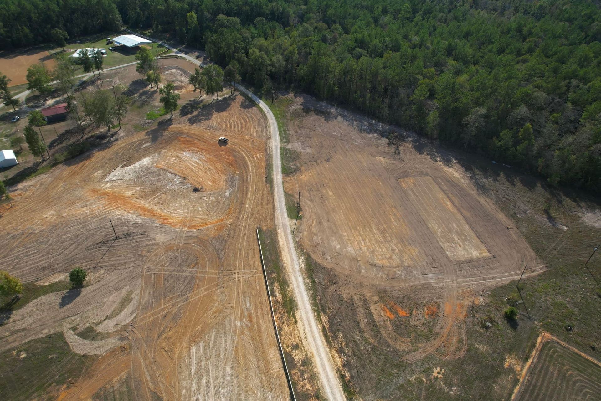 Aerial view of a dirt road through a deforested area with cultivated fields and a treeline.