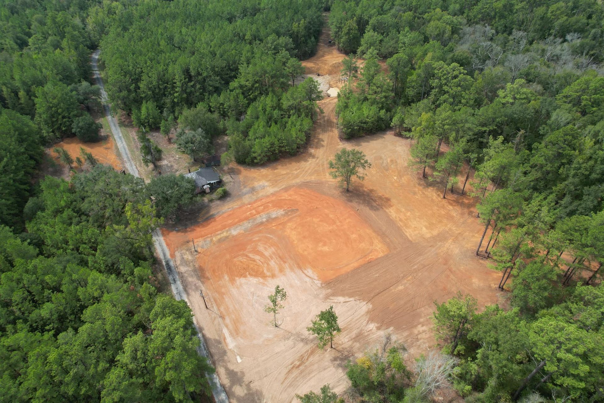 Aerial view: Cleared land bordered by trees, with a small house and road visible.
