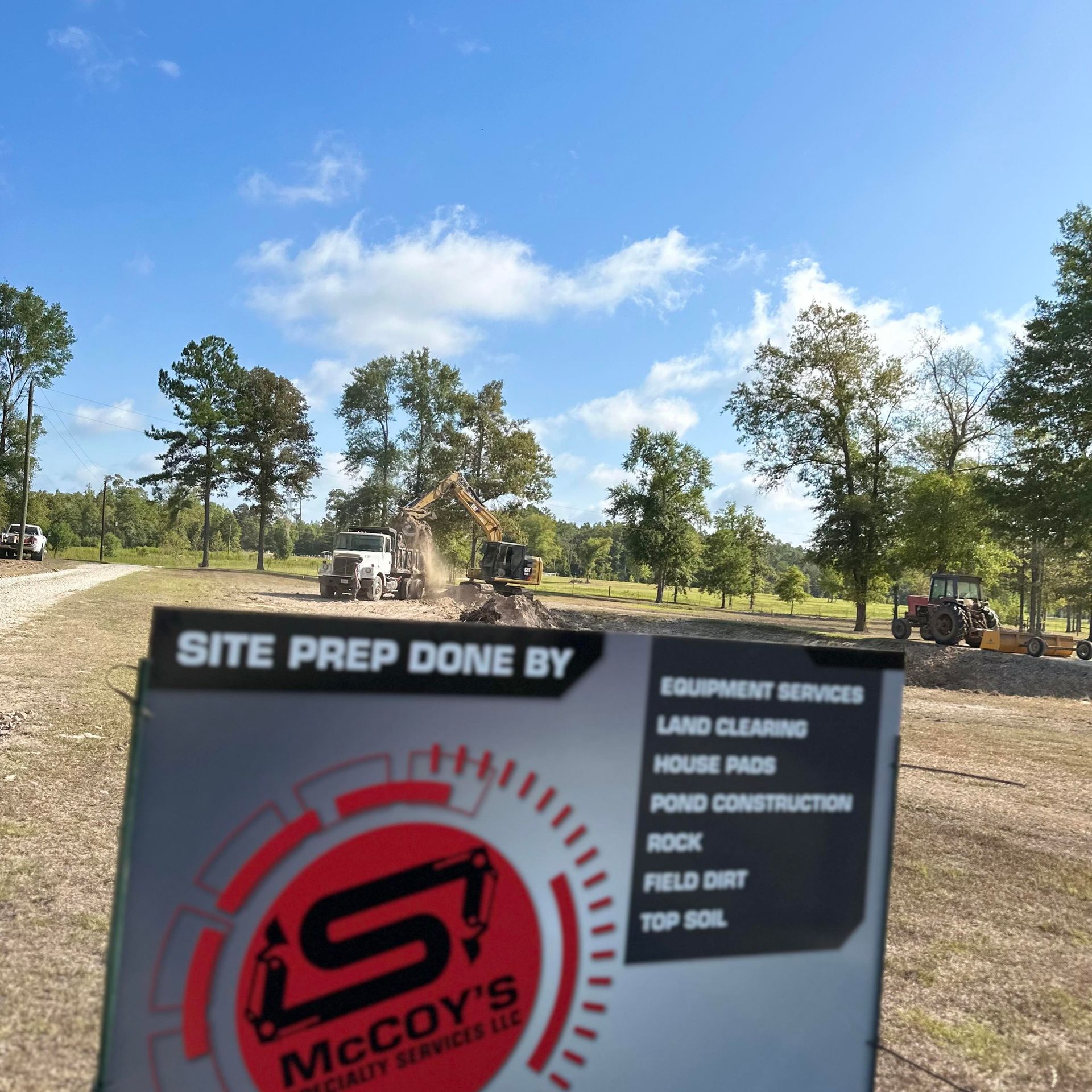 Sign for McCoy's Equipment Services at a construction site. Machinery in the background clearing land under a blue sky.
