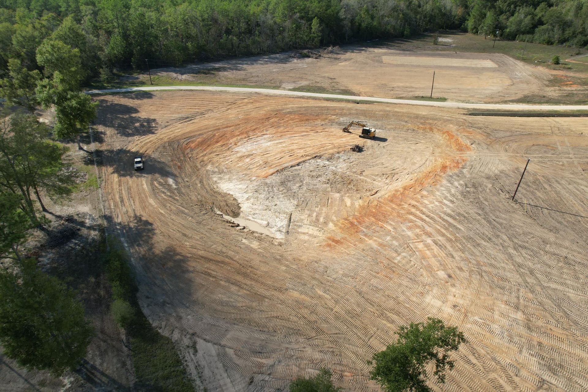 Aerial view of land clearing. A bulldozer and other equipment work on the brown and tan earth. Trees line the perimeter.