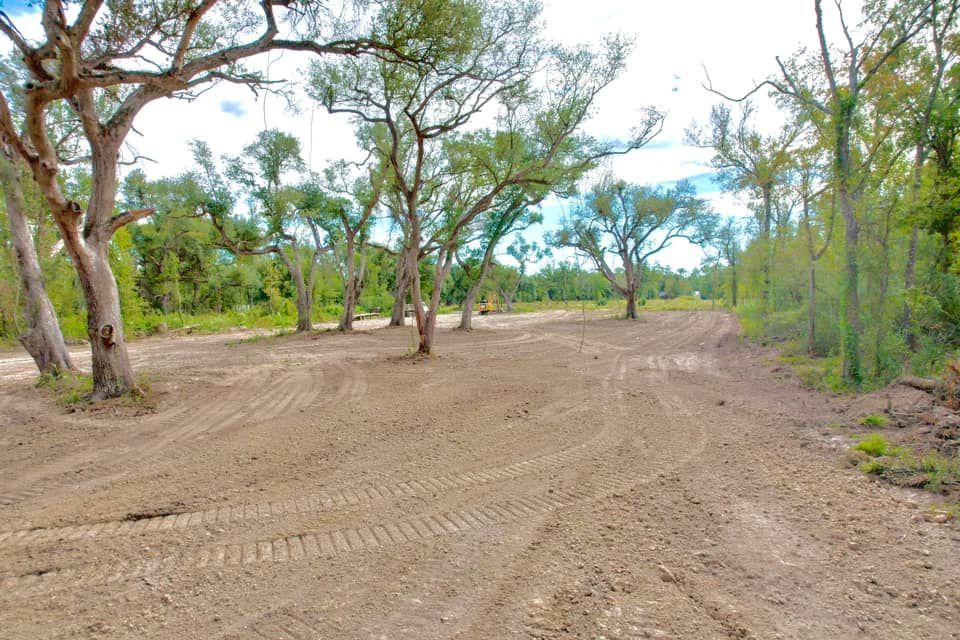 Clearing in a wooded area with trees and tire tracks in the dirt. Blue sky visible.