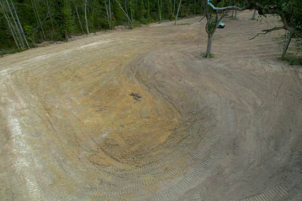 A cleared area of dirt with tire tracks and some trees in the background.