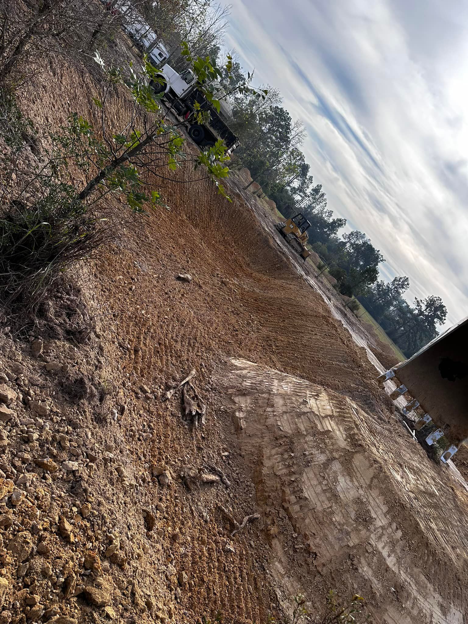 Brown ground covered in gravel, with trees and a cloudy sky in the background.