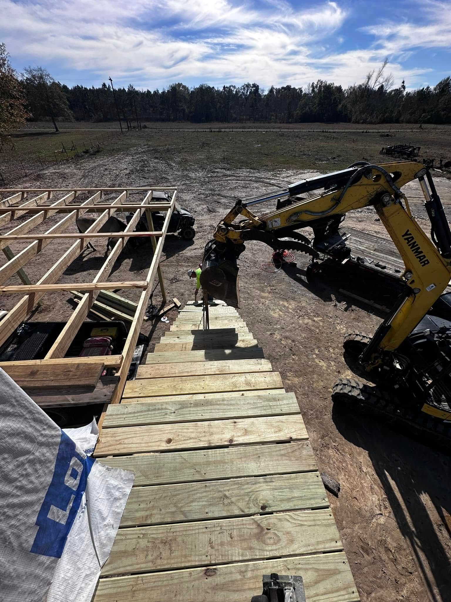 Construction site: excavator digging near a wooden platform and partially built structure; outdoors on a sunny day.