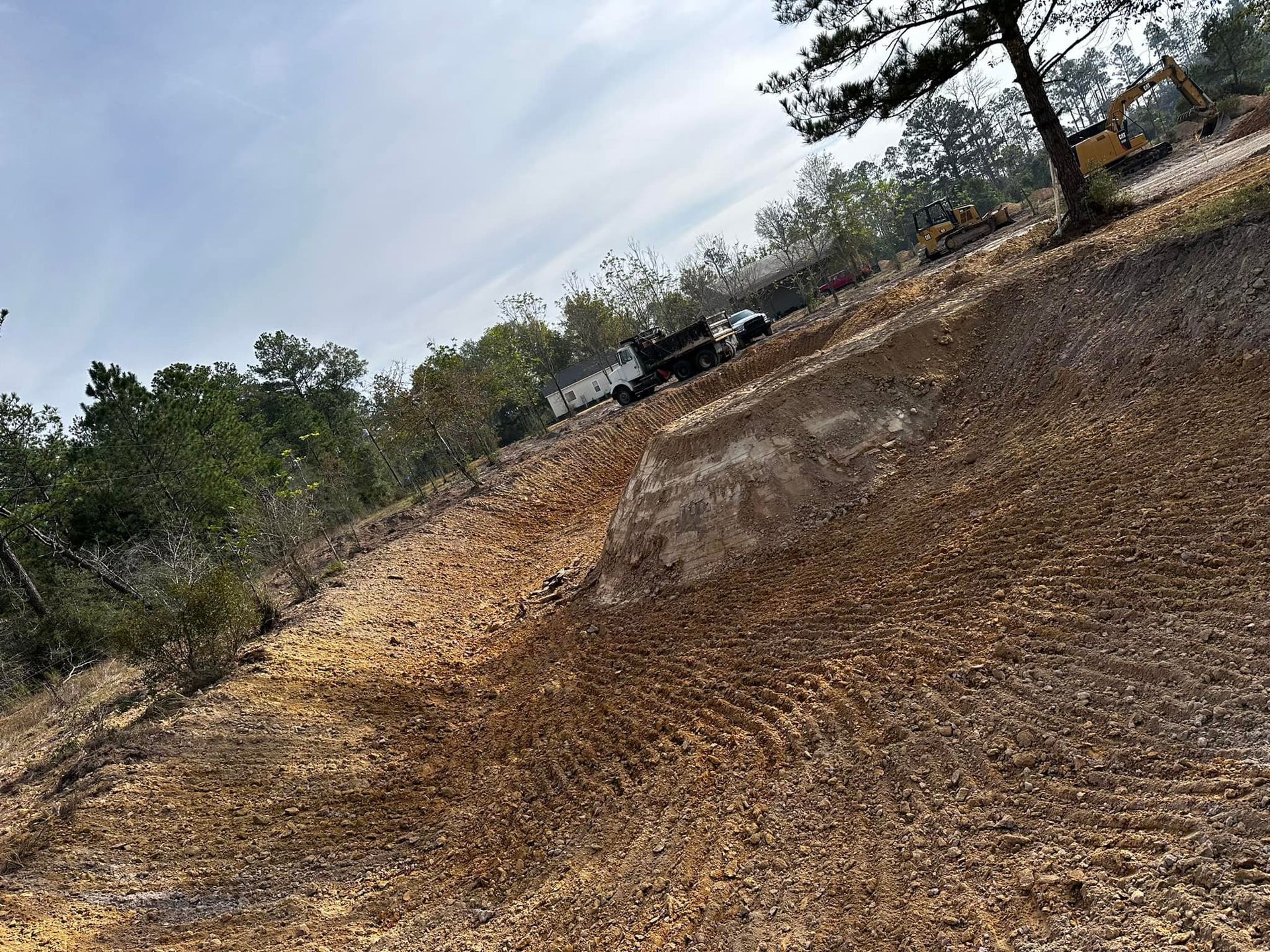 Brown soil slope with a truck and trees under a cloudy sky.