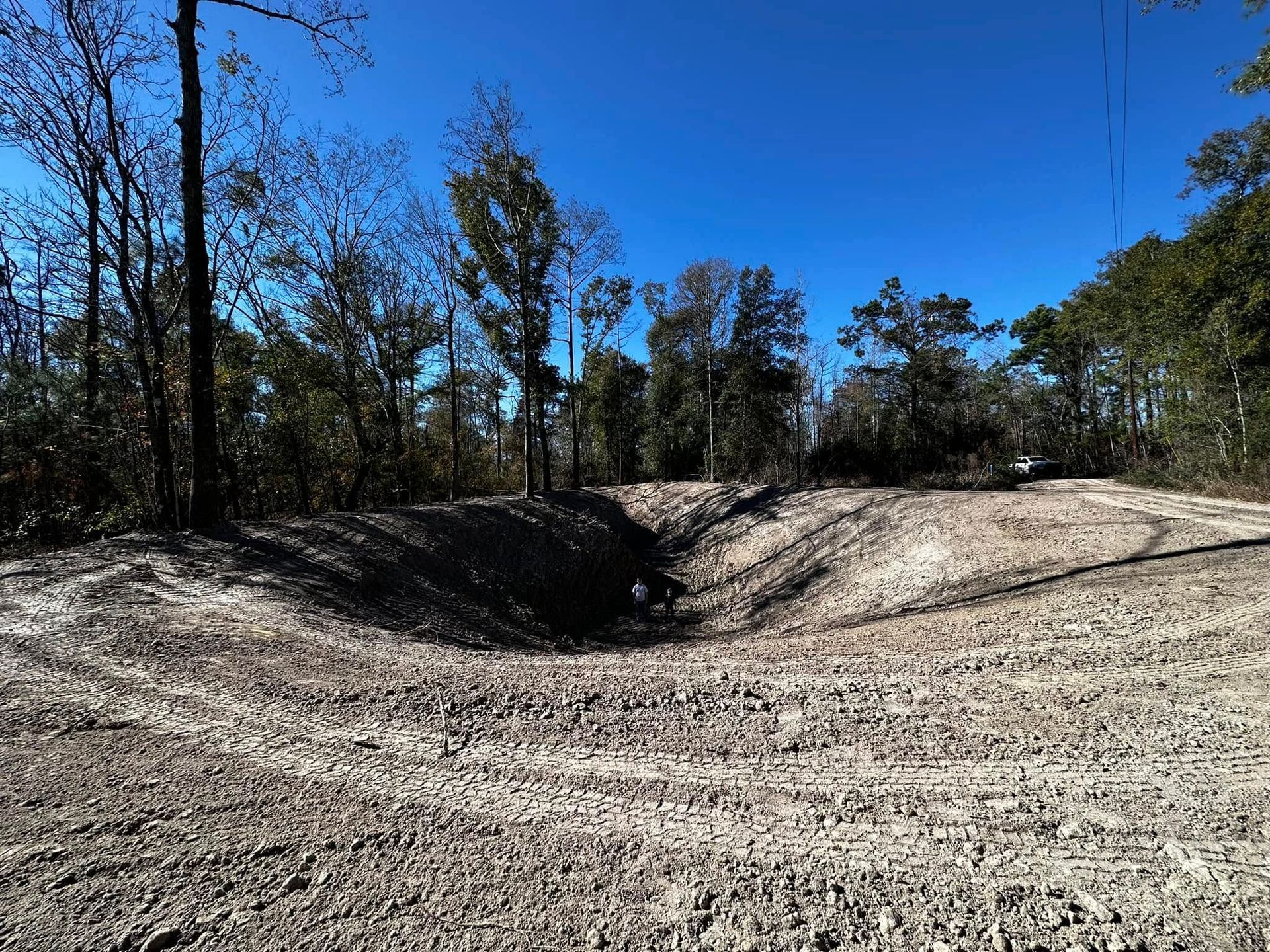 A large, excavated hole in a dirt clearing with trees against a blue sky.
