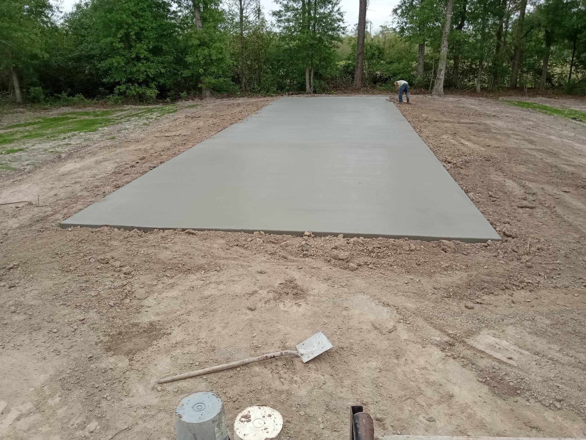 Freshly poured concrete pad surrounded by dirt. A person works in the background.