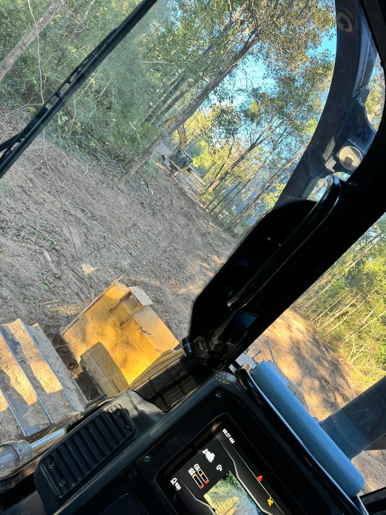 View from inside a heavy machinery cab, looking out at a forest clearing.
