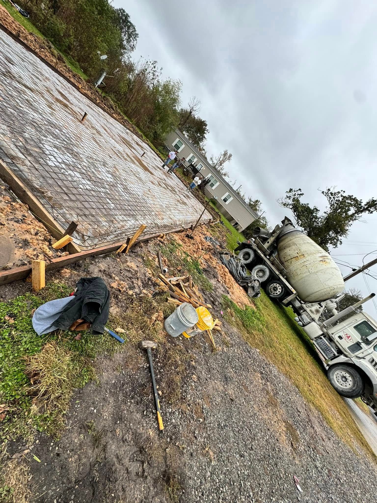 Concrete truck pouring cement into a prepared foundation. Tools and debris are scattered nearby on a cloudy day.