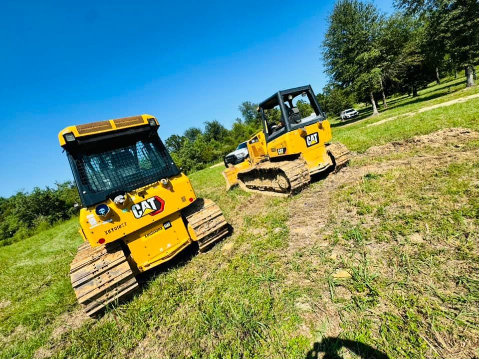 Two yellow Caterpillar compact track loaders on grassy slope under blue sky.