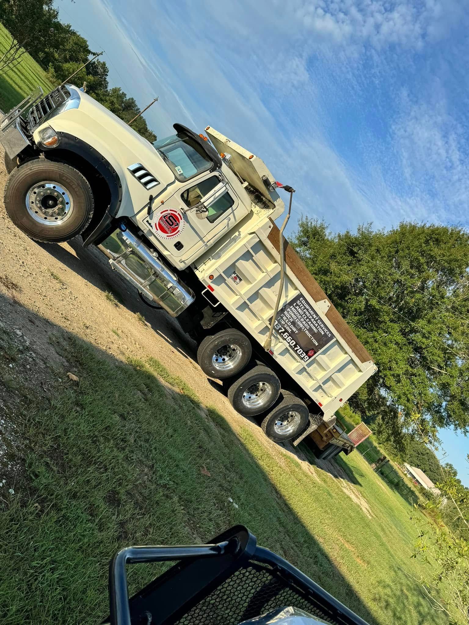 Beige dump truck parked on grass, angled against a blue sky.