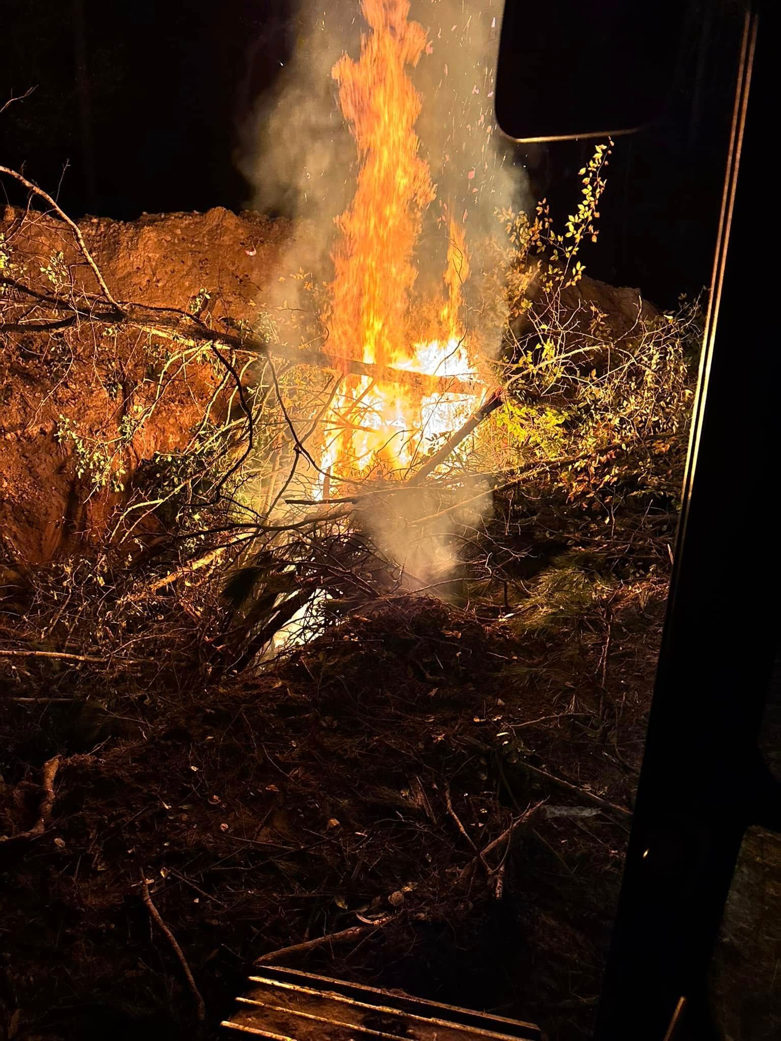 Fire burning brightly in a pile of brush at night. Sparks and smoke rise against the darkness.