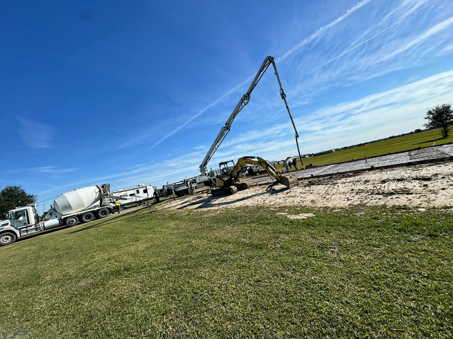 Construction site with concrete trucks and a pump pouring cement on a roadway under a blue sky.
